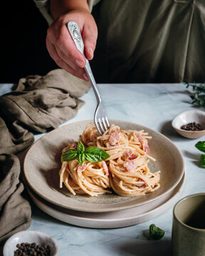 Hand twirling fork in creamy pasta dish with basil garnish