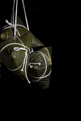 Rice dumpling zongzi hanging over black background a aditional sweet Chinese food for Dragon Boat Duanwu Festival celebration - dark and moody