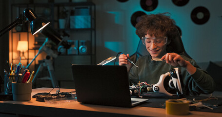 A focused child sits at a desk, watching instructional videos on a laptop. Inspired by creators, the child solders a robot, connects wires, and builds a simple electrical system.