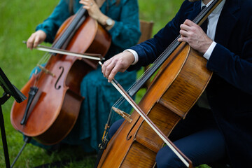 Fototapeta premium A close-up view of a woman in a teal dress playing the cello on grass, highlighting the instrument, bowing technique, and elegant attire
