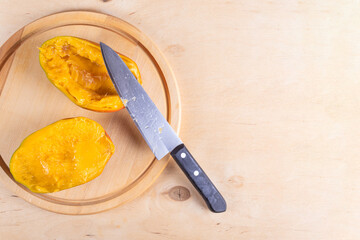 Top view of two halves of mango and kitchen knife on wooden background
