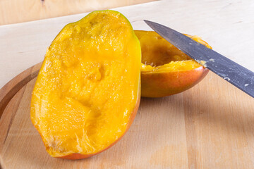 Side view of two halves of mango and kitchen knife on wooden background