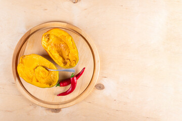 Top view of two halves of mango, two red hot chili peppers and spoon on wooden background with copy space
