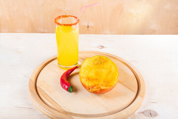 Glass of mangonada, half of mango and red hot chili pepper on wooden background