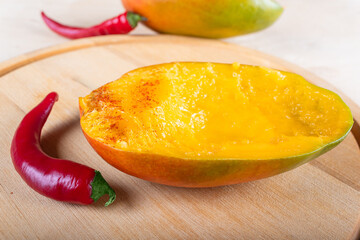 Side view of two halves of mango and two red hot chili peppers on wooden background, close-up