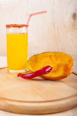 Glass of mangonada, half of mango and red hot chili pepper on wooden background