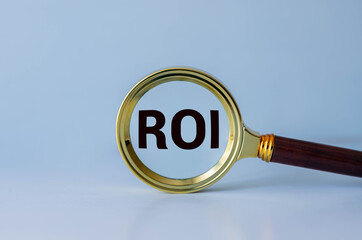 Three wooden cubes with the word ROI on graph sheets, abbreviation for Return on Investment, Magnifying glass focusing on ROI letters, Return on investment business concept, Financial growth and analy