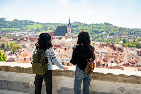Two young female tourists with backpacks admire a breathtaking panoramic view of Cesky Krumlov, a historic town in South Bohemia, Czech Republic. travel, tourism, Europe, female travelers, friendship