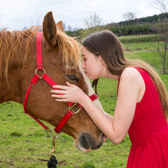 A young woman in a red dress kissing her horse