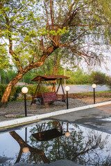 Wooden swing under the tree in the park with reflection in water