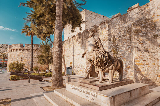 28 April 2025, Cesme, Turkiye: Stone statue of Cezayirli Gazi Hasan Pasha, an Ottoman admiral, posing next to a lion with Cesme Castle