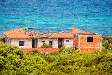 Crumbling walls and broken roof of an abandoned house by the tranquil blue sea, evoking a sense of...