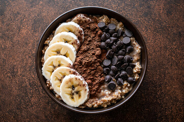 Oatmeal porridge with banana slices, chocolate chips, and cocoa powder topping