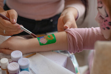selective focus. decorative cosmetics for children and adults. holy Flash tattoo. Transfer tattoos for kids. master makes a girl a transfer temyporar glitter tattoo with sequins. childreay. Animators