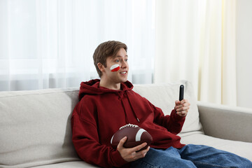 Emotional sports fan with remote control and ball watching game indoors