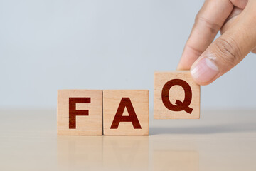 Hand holding wooden cube blocks with FAQ text (frequently asked questions) on table background....