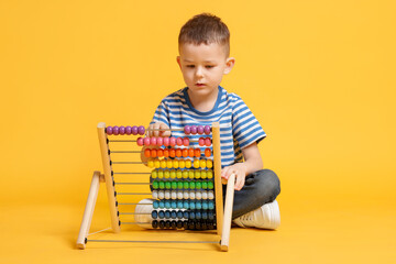 Cute little boy playing with wooden abacus on yellow background