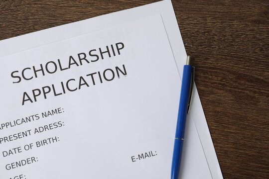 Scholarship application form and pen on wooden table, top view