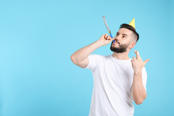 Happy Birthday. Handsome man with party hat and blower crossing fingers while making wish on light...