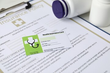 Health insurance card, policy and medical bottles on white table, closeup
