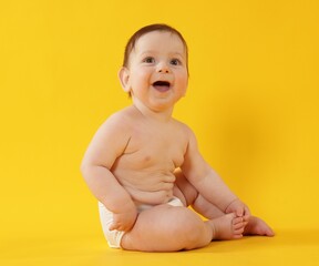 Cute little baby in diaper sitting on yellow background