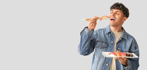 Young man eating tasty sushi on light background with space for text