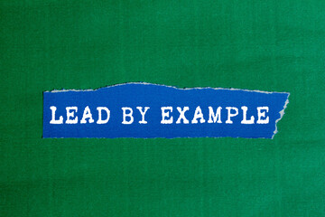 Lead by example message written on ripped torn blue paper piece on green background. Conceptual...