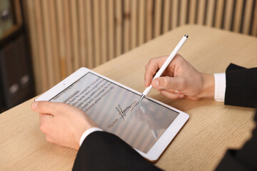 Electronic signature. Man using stylus and tablet at wooden table, closeup