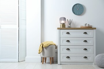 Dresser with stylish reed diffuser and lamp near white wall indoors