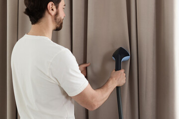 Man steaming curtains with stand steamer at home