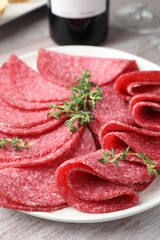 Slices of delicious sausage with thyme served on light wooden table, closeup