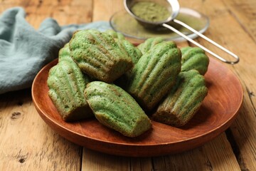 Tasty madeleine cakes and matcha powder on wooden table, closeup