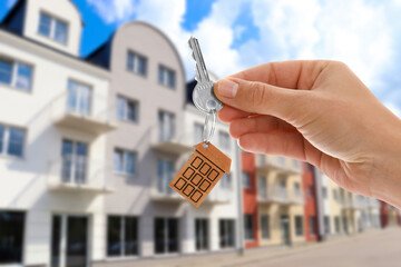Real estate agent holding house key against buildings outdoors, closeup