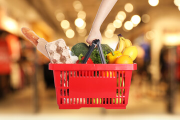 Woman holding shopping basket with different food products at supermarket, closeup