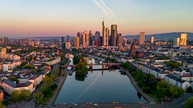 Aerial sunrise hyper time lapse view of the skyline of Frankfurt, Germany, and River Main with golden sunlight