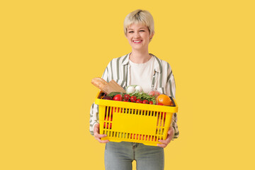 Young woman with full shopping basket on yellow background