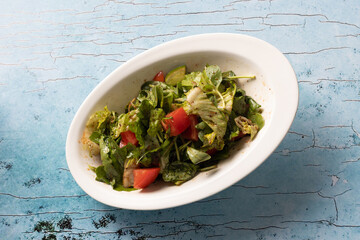 Fresh mixed green salad with tomatoes in white oval bowl.
