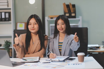 Two young Asian business woman talk, consult, discuss working with new startup project idea presentation analyze plan marketing and investment in the office.