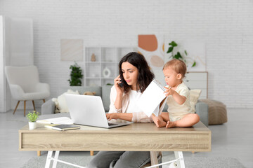 Cute little baby and young mother working with laptop while talking by mobile phone on maternity...