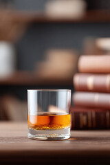 A tumbler of amber liquor rests on a wooden table near a stack of books. Evokes relaxation, refinement, or study. Ideal for lifestyle, culture, or beverage themes.