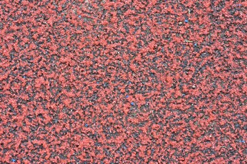 Red sports field rubber coating close up macro view. Playground paving background texture extremely...