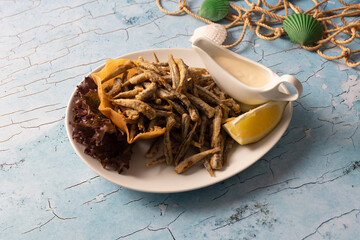 Crispy fried anchovies served with lemon, sauce, and garnish.