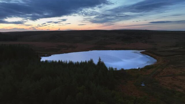 Bragan, County Monaghan, Ireland, September 2022. Drone tracking right over dense forest establishes Lake Menish pulling back across bog wetlands at blue hour twilight dusk light.