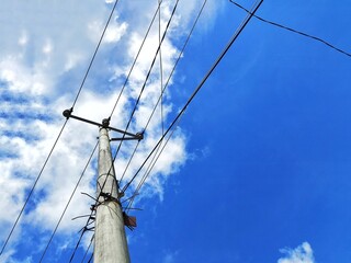 Electric pole with multiple power lines stretching across a bright blue sky with scattered clouds....