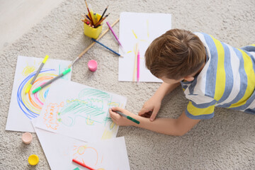 Little boy drawing dinosaur with felt-tip pens on floor at home