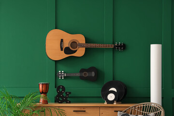 Commode with vinyl disks and musical instruments near green wall