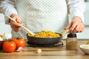 Woman preparing pilaf in frying pan on table, closeup