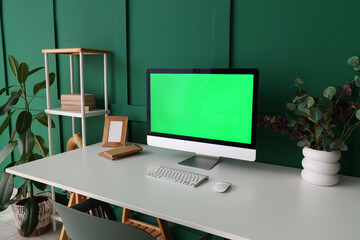 Modern workplace with computer and shelving unit near green wall in room