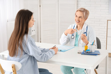 Fototapeta premium Happy mature female doctor giving pills to patient in clinic
