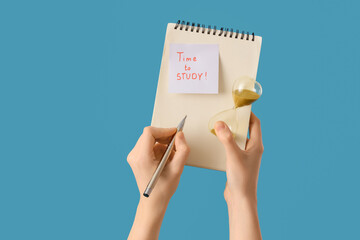 Woman holding notebook with text TIME TO STUDY and hourglass on blue background
